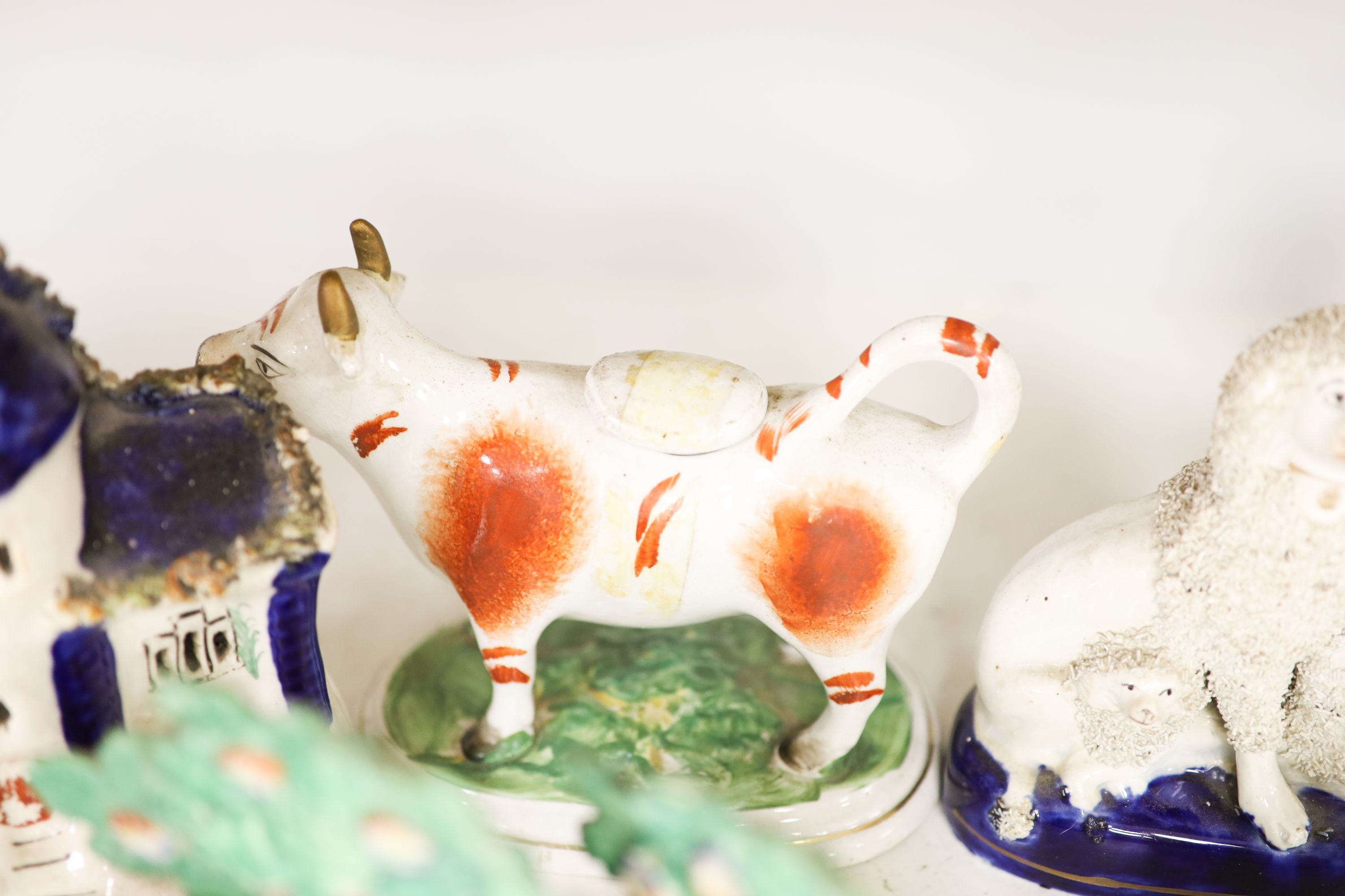 A collection of Victorian Staffordshire pottery to include a sponge glazed seated cat, a pair of bocage sheep, cow creamer etc (14).